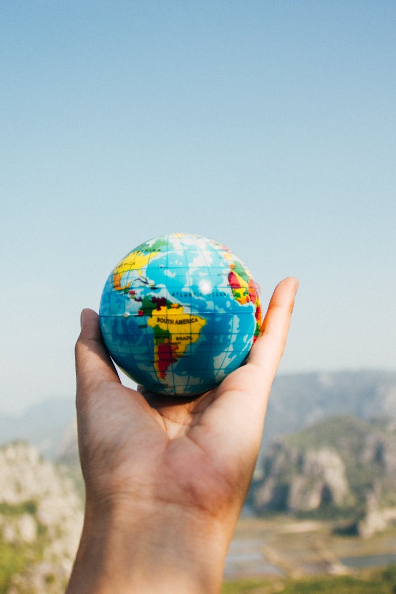 Hand holding a globe against a mountain background symbolizing travel and exploration.